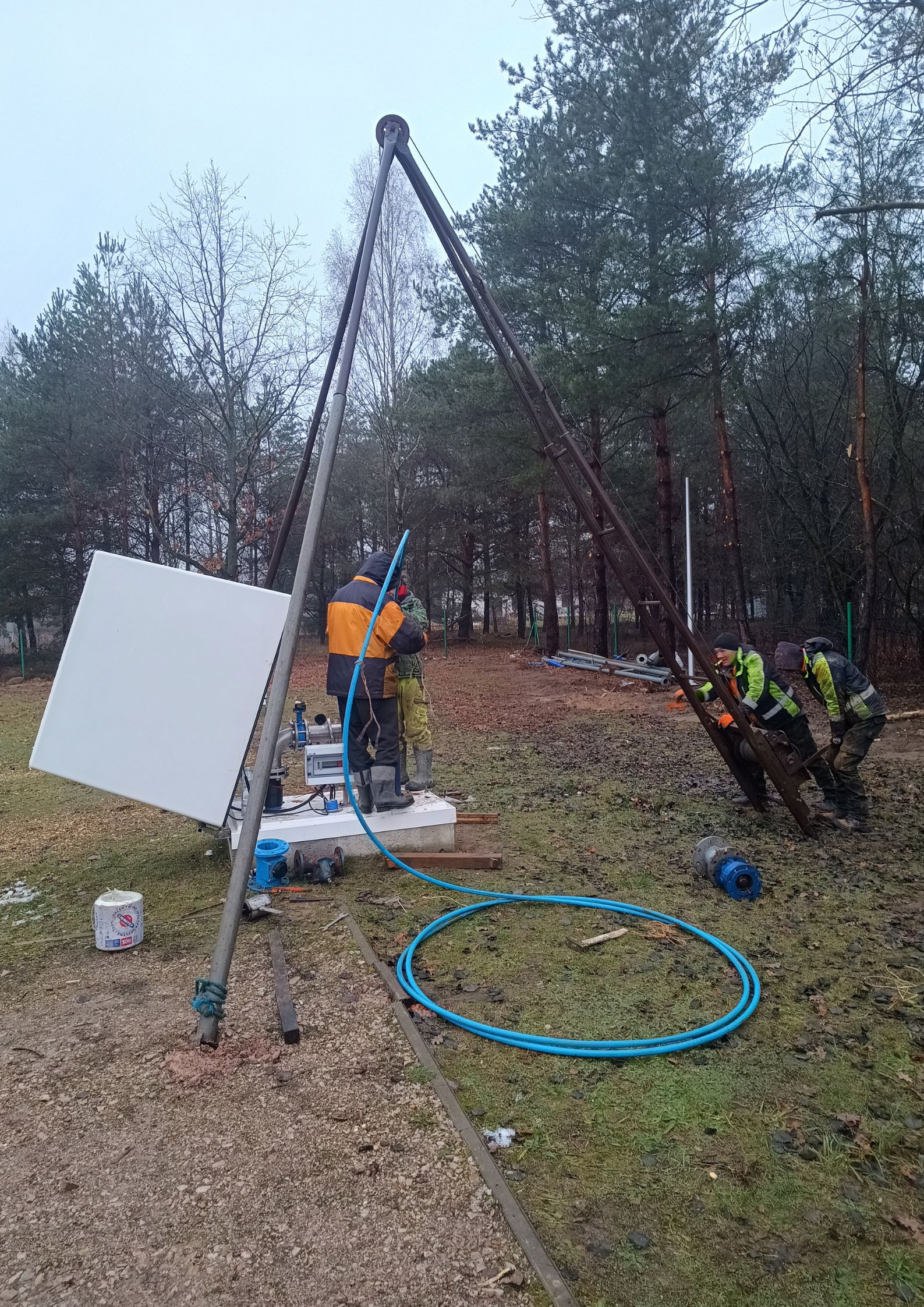 Czyszczenie studni na terenie SUW Lipowo. DWóch Panów stoi na studni głębinowej, dwóch trzyma nogi żurawia technicznego.