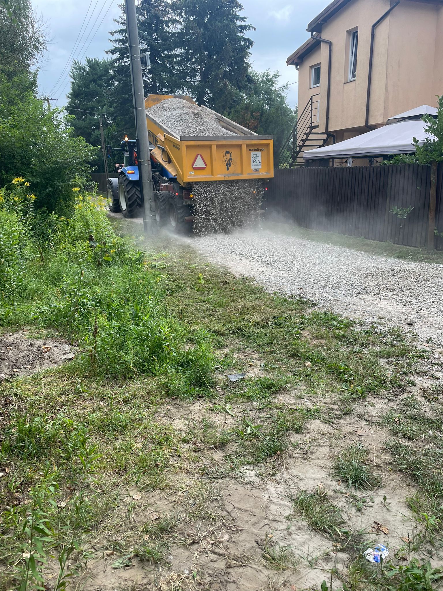 W tle znajduje się traktor New Holland, z którego przyczepy wysypywane jest kruszywo