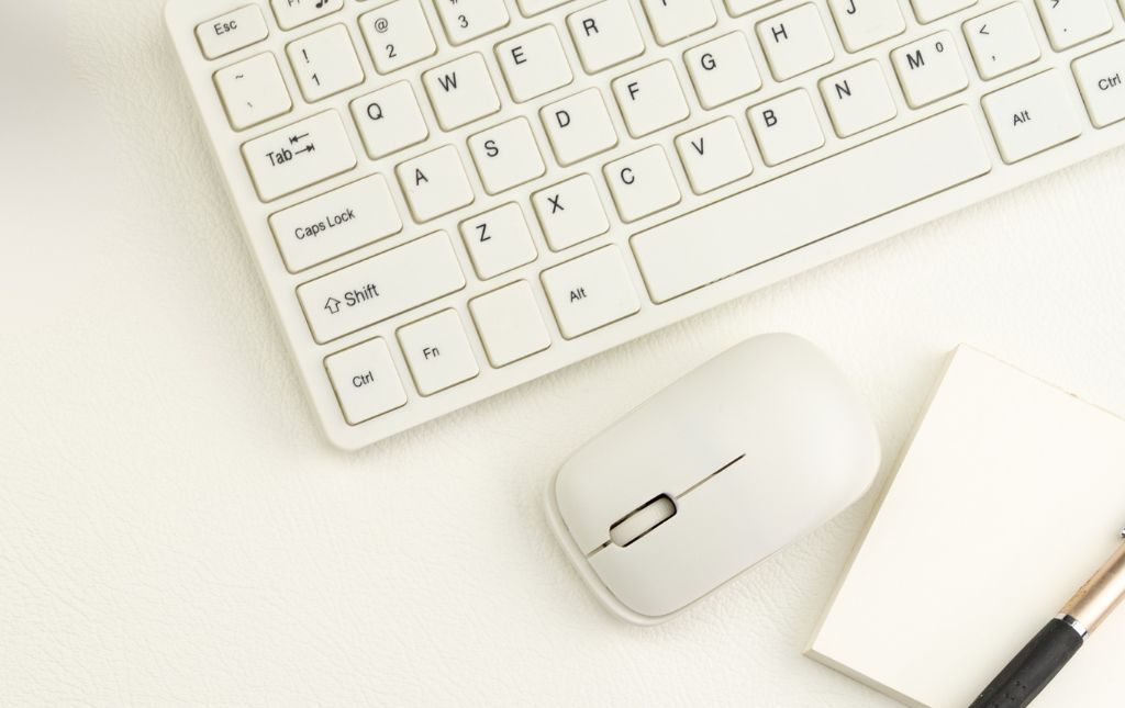 Na fotografii widać część klawiatury, myszkę oraz notes.